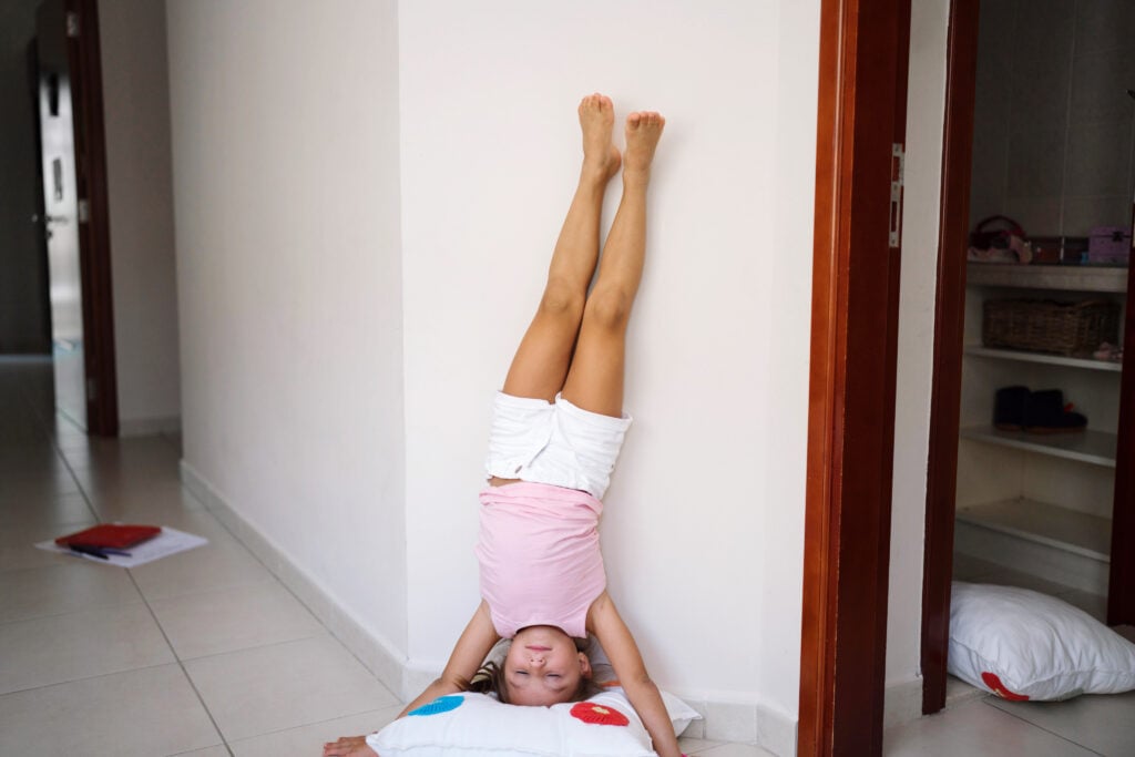 Little girl doing a headstand at home, upside down against the wall,  for vestibular input and proprioceptive input. 