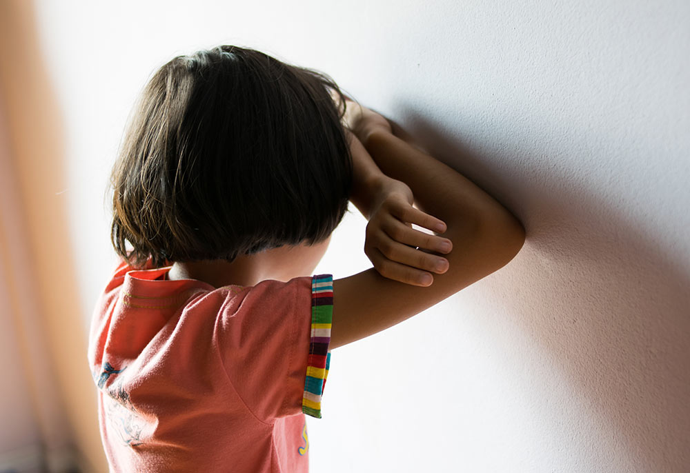 a child standing in the corner with their face against the wall in a time out.